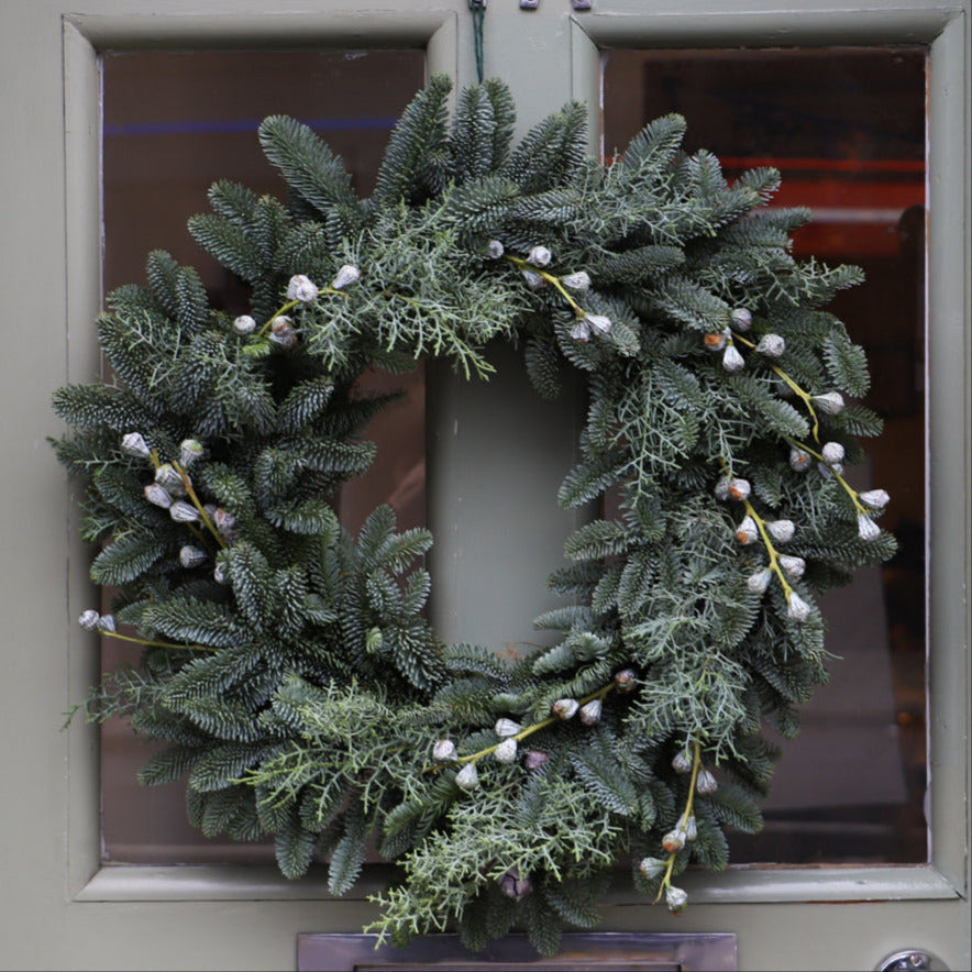 A pine wreath decorated with eucalyptus pods shown hanging on a front door