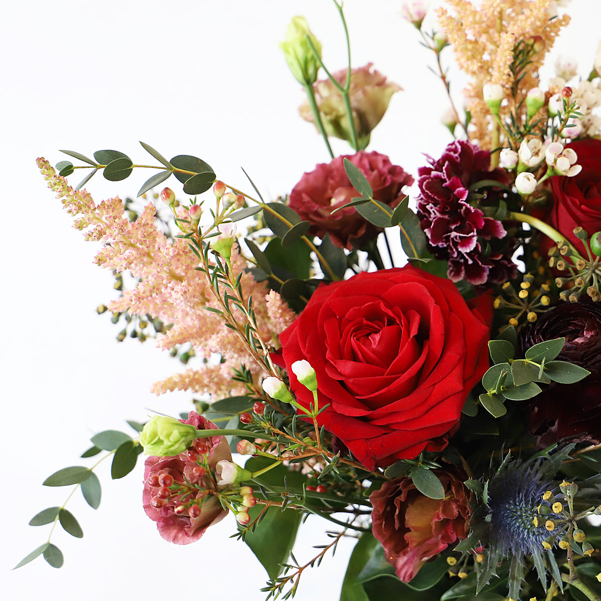 A detail picture of a red rose with pink and burgungy flowers