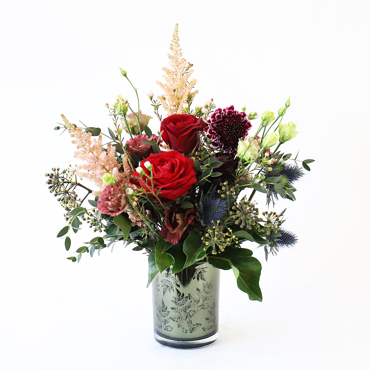 A small bouquet of red roses with pink and deep burgurgy flowers in a glass vase