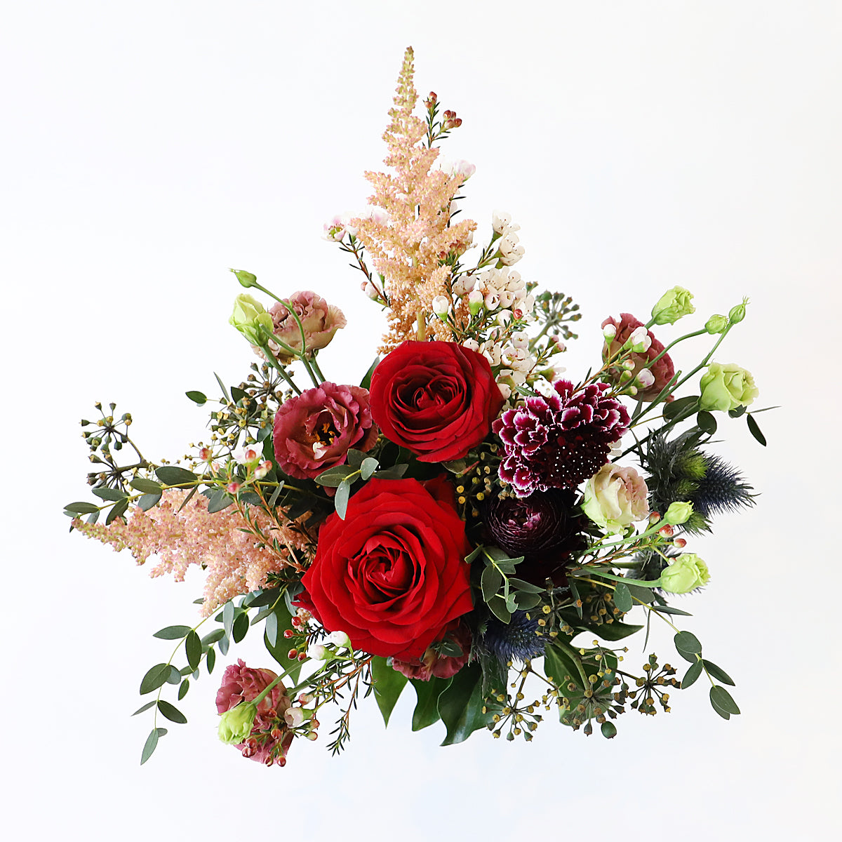 A top view of a small bouquet of red roses with pink and deep burgurgy flowers