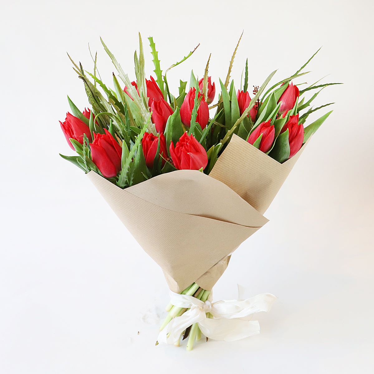 A bouquet or red tulips with foliage wrapped in brown paper and tied with a ribbon