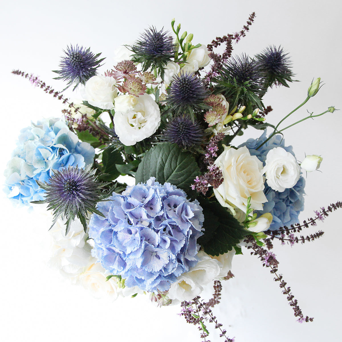 Over head view of blue and white hydrangeas, thistle and white lisianthus