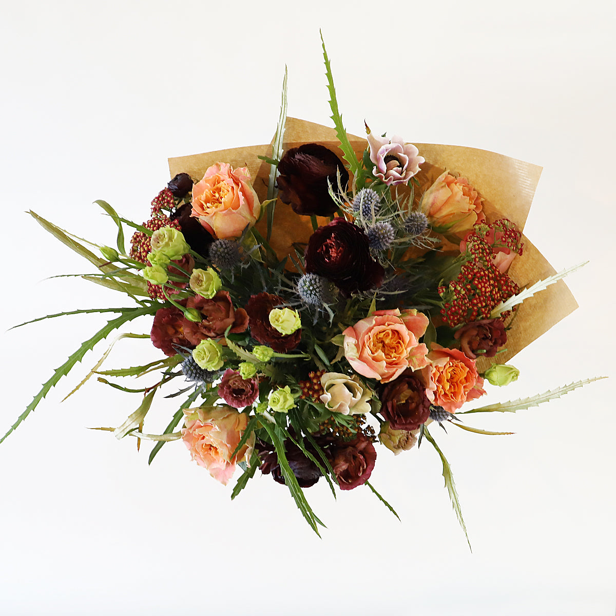 Overhead view of the bouquet with orange rose, blue thistle and other burgundy flowers wrapped in brown paper