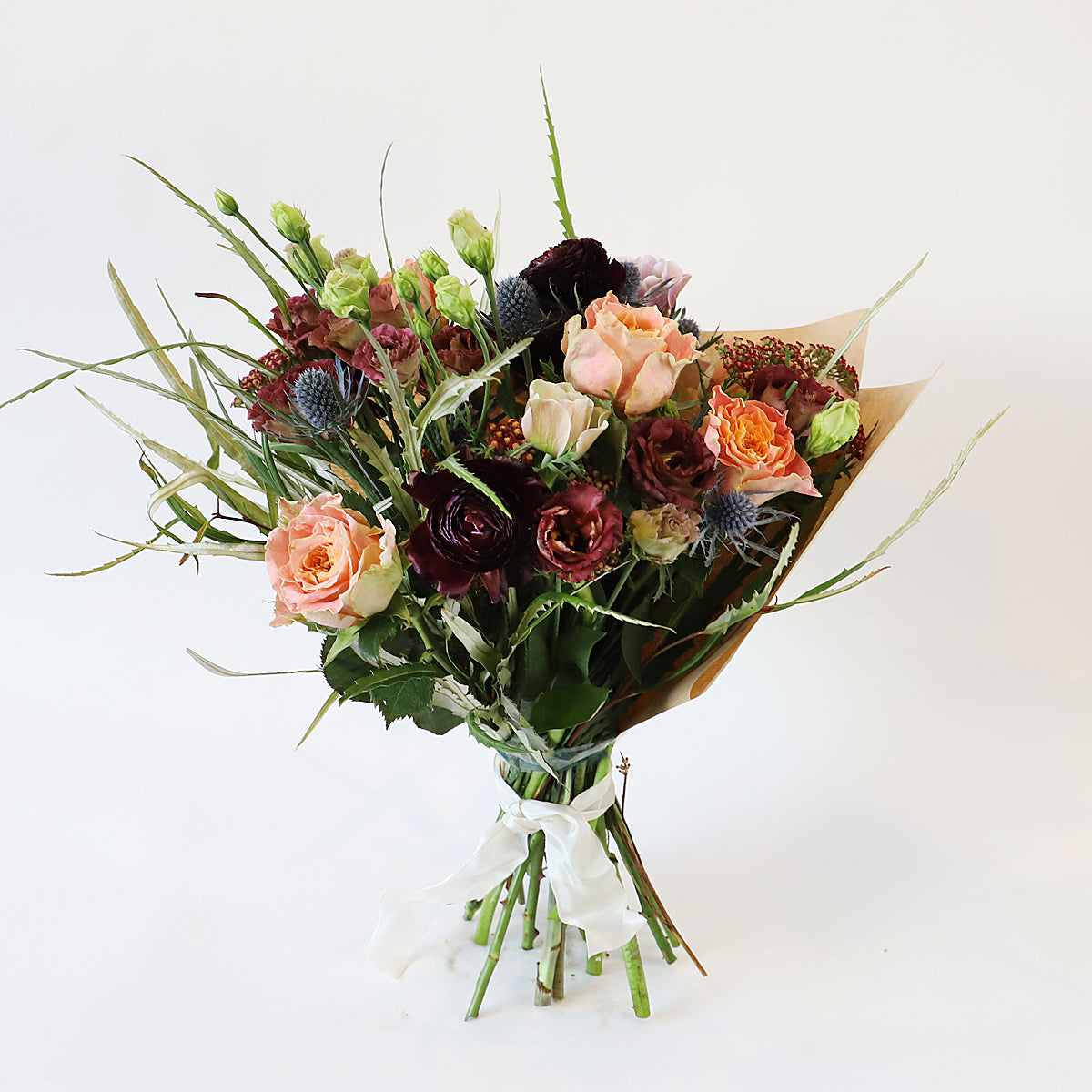 A bouquet with orange roses, blue thistle and other burgundy flowers with foliage