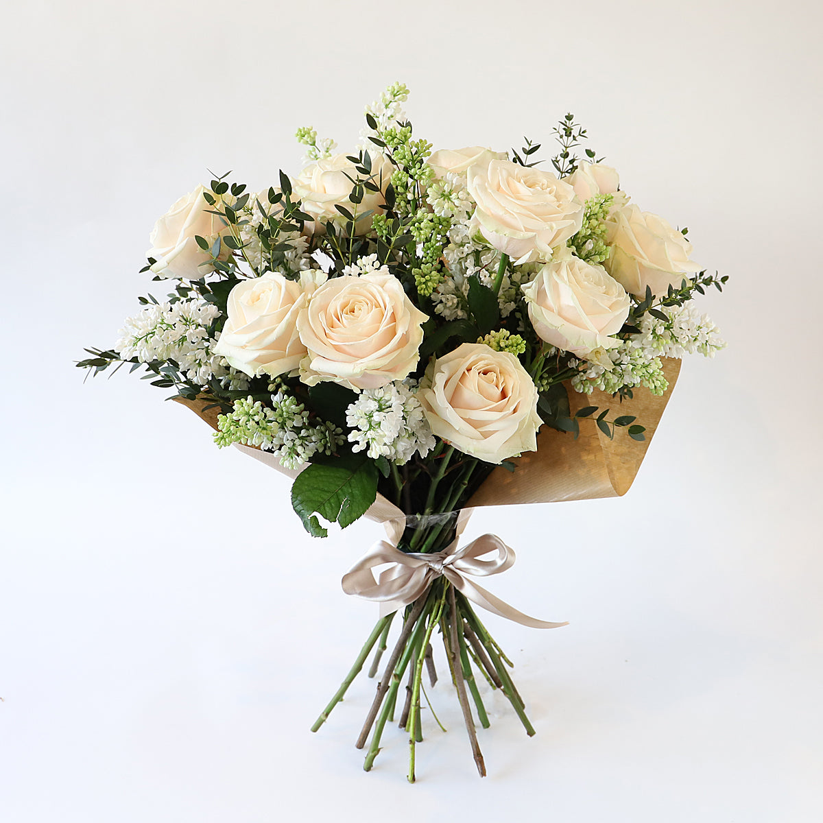 A bouquet of cream roses, white lilac and eucalyptus foliage wrapped in brown paper