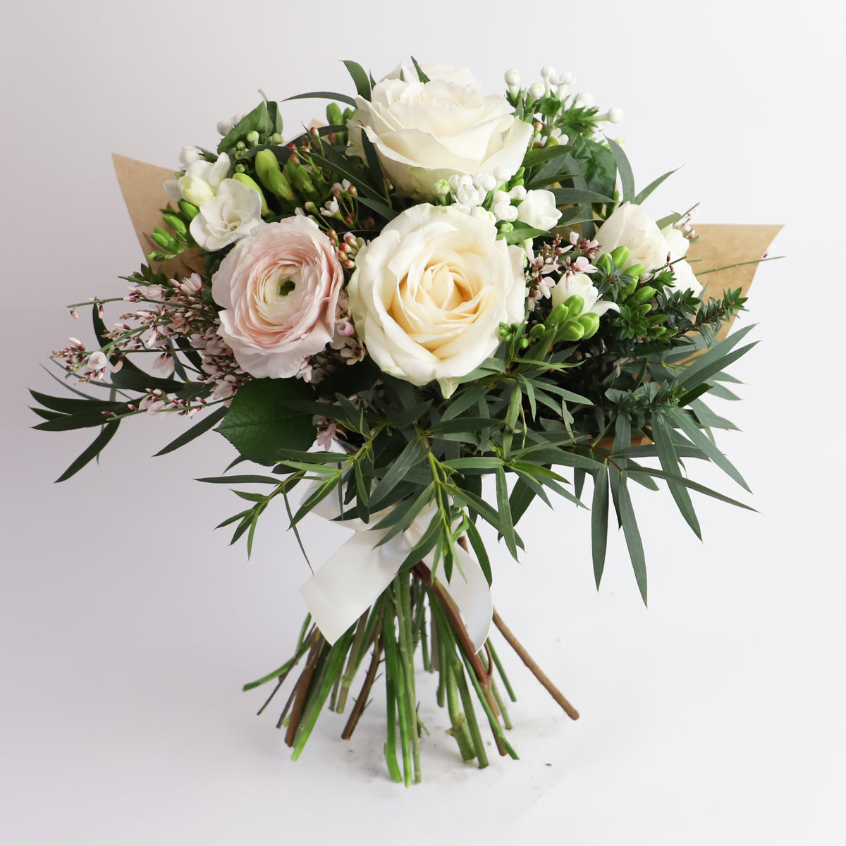 A bouquet of cream roses and pale pink ranunulus with fressis and foliage wrapped in brown paper