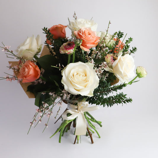 A bouquet containing peach and cream roses with ranunulus and foliages