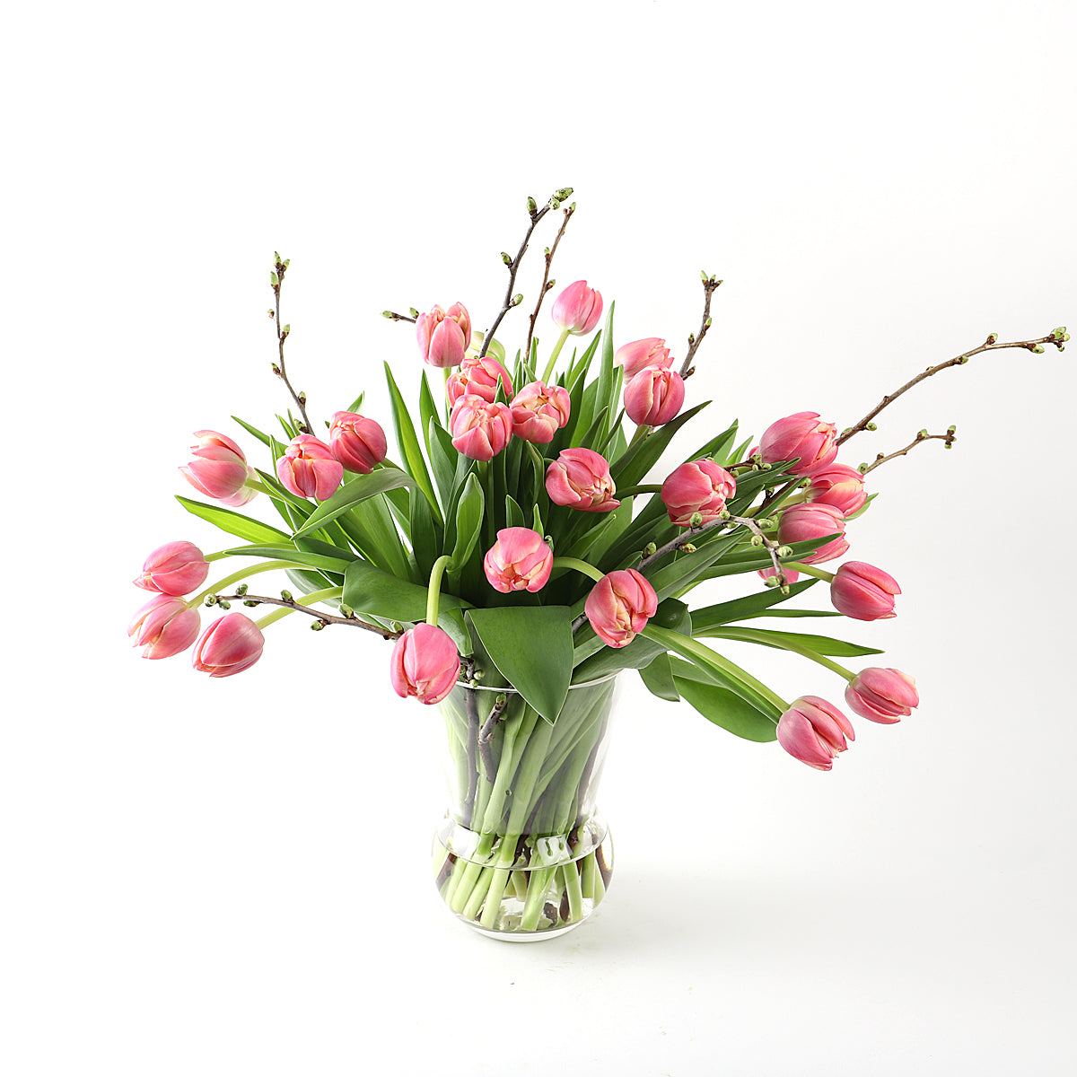 A bouquet of pink tulips and pussy willow in a glass vase