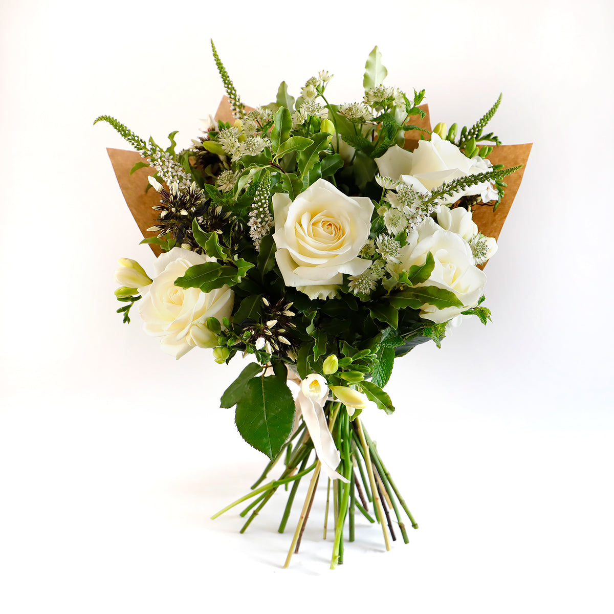 A bouquet with white roses, white veronica, white freesia and astrantia wrapped in brown paper