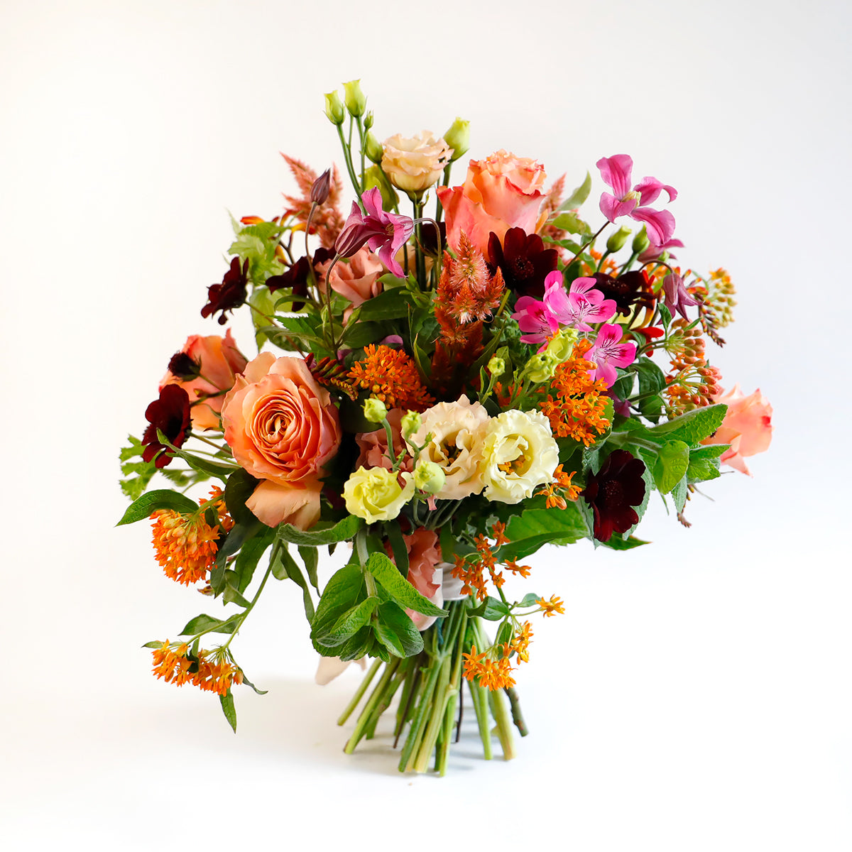 A large bouquet of coral roses, cream lisianthus, pink clemetis and other orange flowers