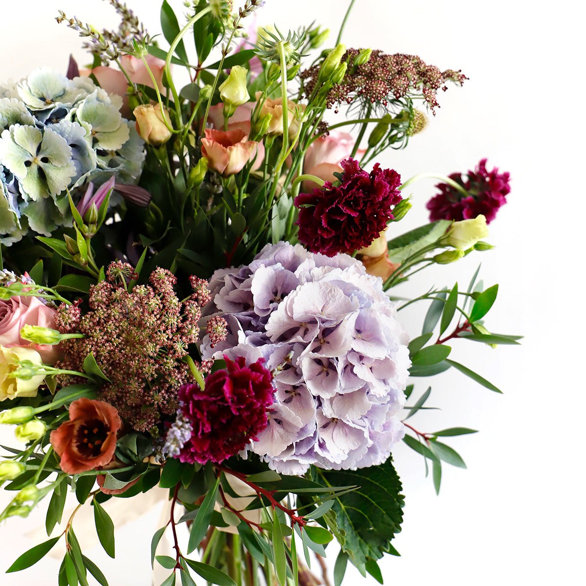 Detail close up of blue hydrangeas, dark pink lisianthus, burgundy stocks and foliage 