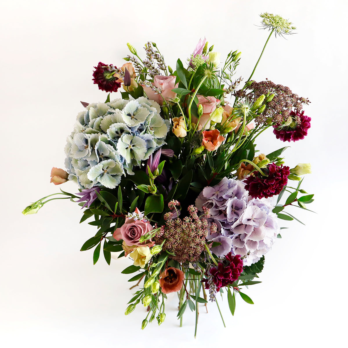 Overhead shot of blue hydrangeas, dark pink lisianthus, burgundy stocks and foliage 