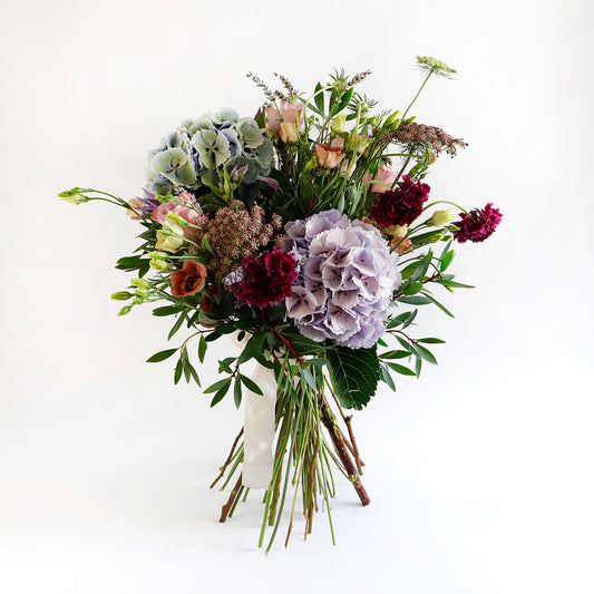 A large bouquet of blue hydrangeas, dark pink lisianthus, burgundy stocks and foliage 