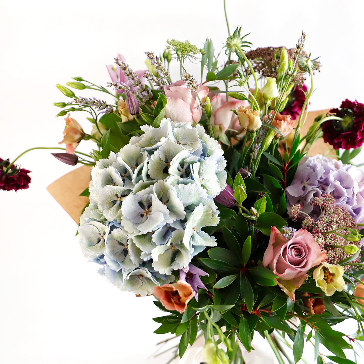 Detail close up of blue hydrangeas, dark pink lisianthus, burgundy stocks and foliage 