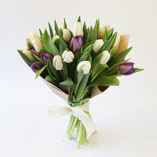 A bouquet of white and purple tulips wrapped in brown paper