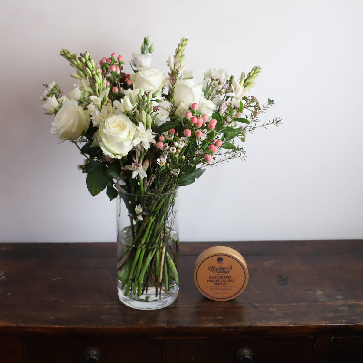 Bouquet of white roses, pink hypericum and tuberose in a vase with a box of chocolates