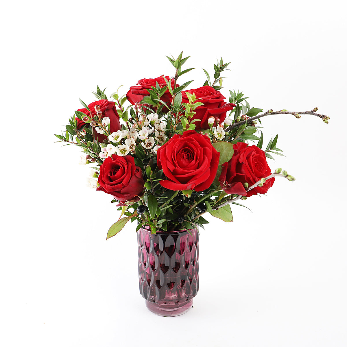 A small bouquet of six red roses and foliage in a glass vase