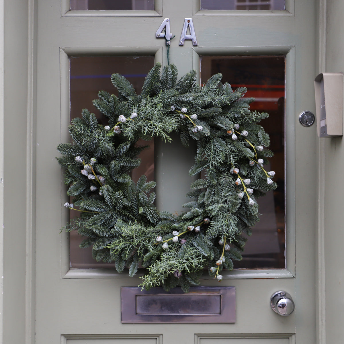 A pine wreath decorated with eucalyptus pods shown hanging on a front door