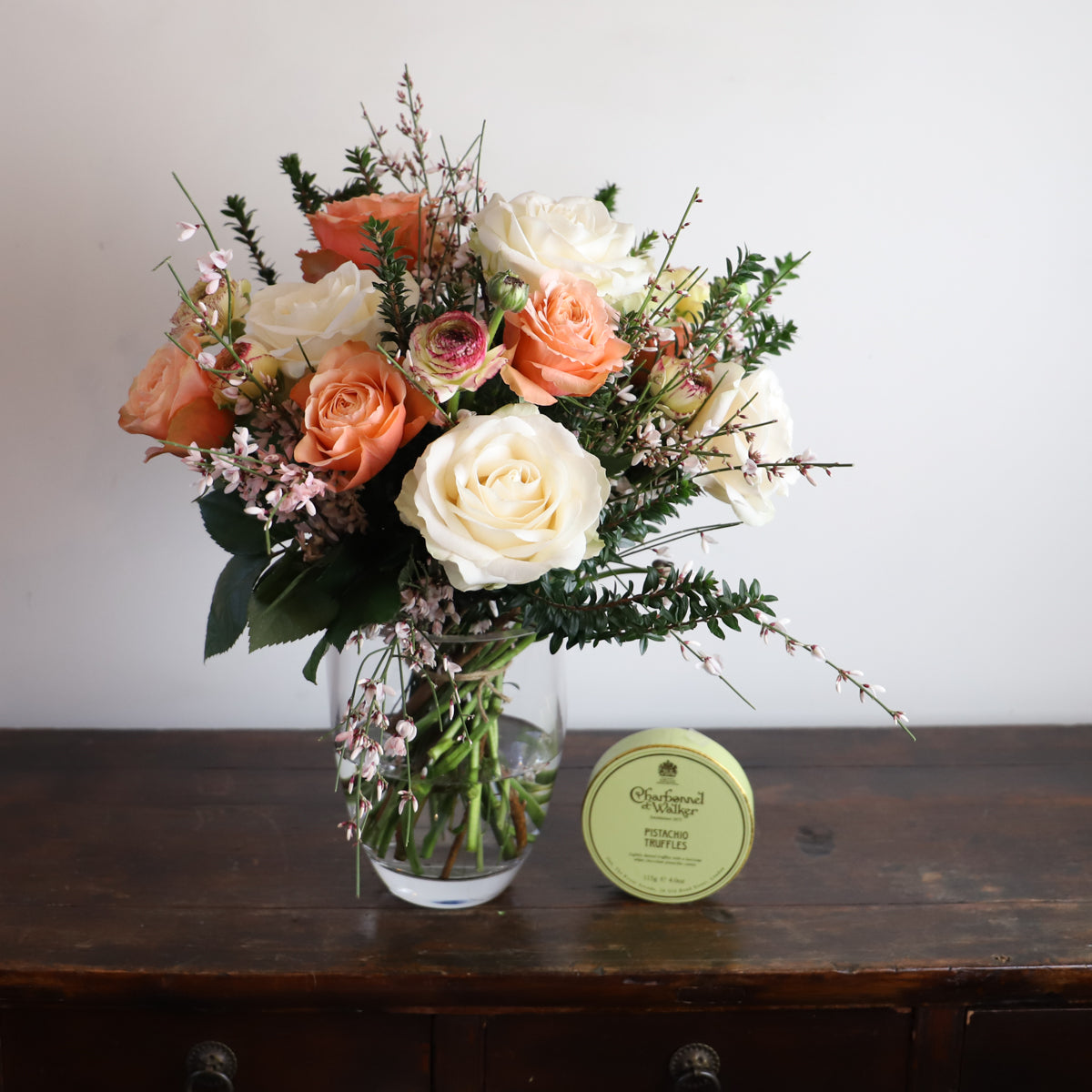 cream and orange bouquet in a vase with a box of chocolates next to it