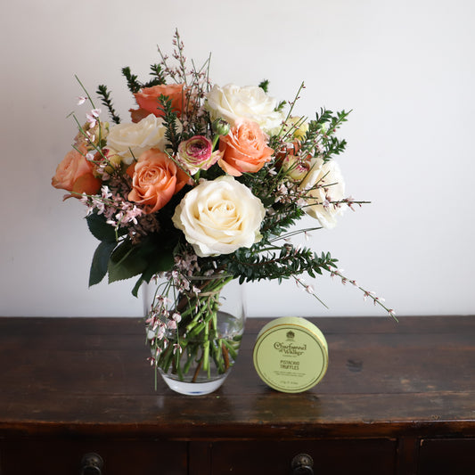 cream and orange bouquet in a vase with a box of chocolates next to it
