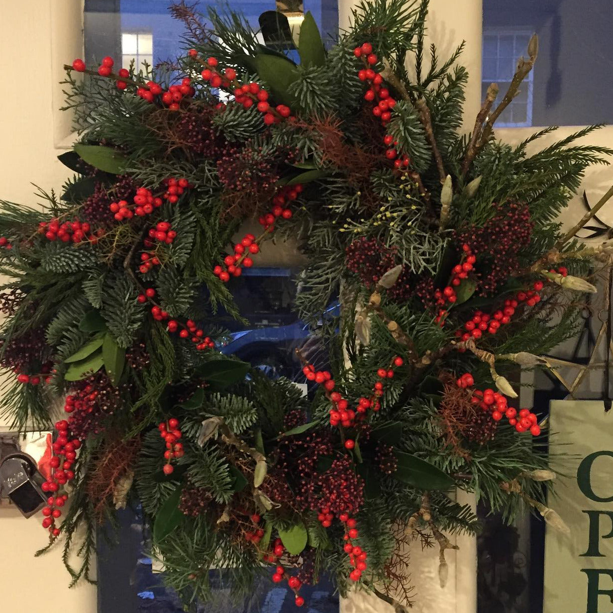 Decorative wreath with red berries on a door with an 'Open' sign.