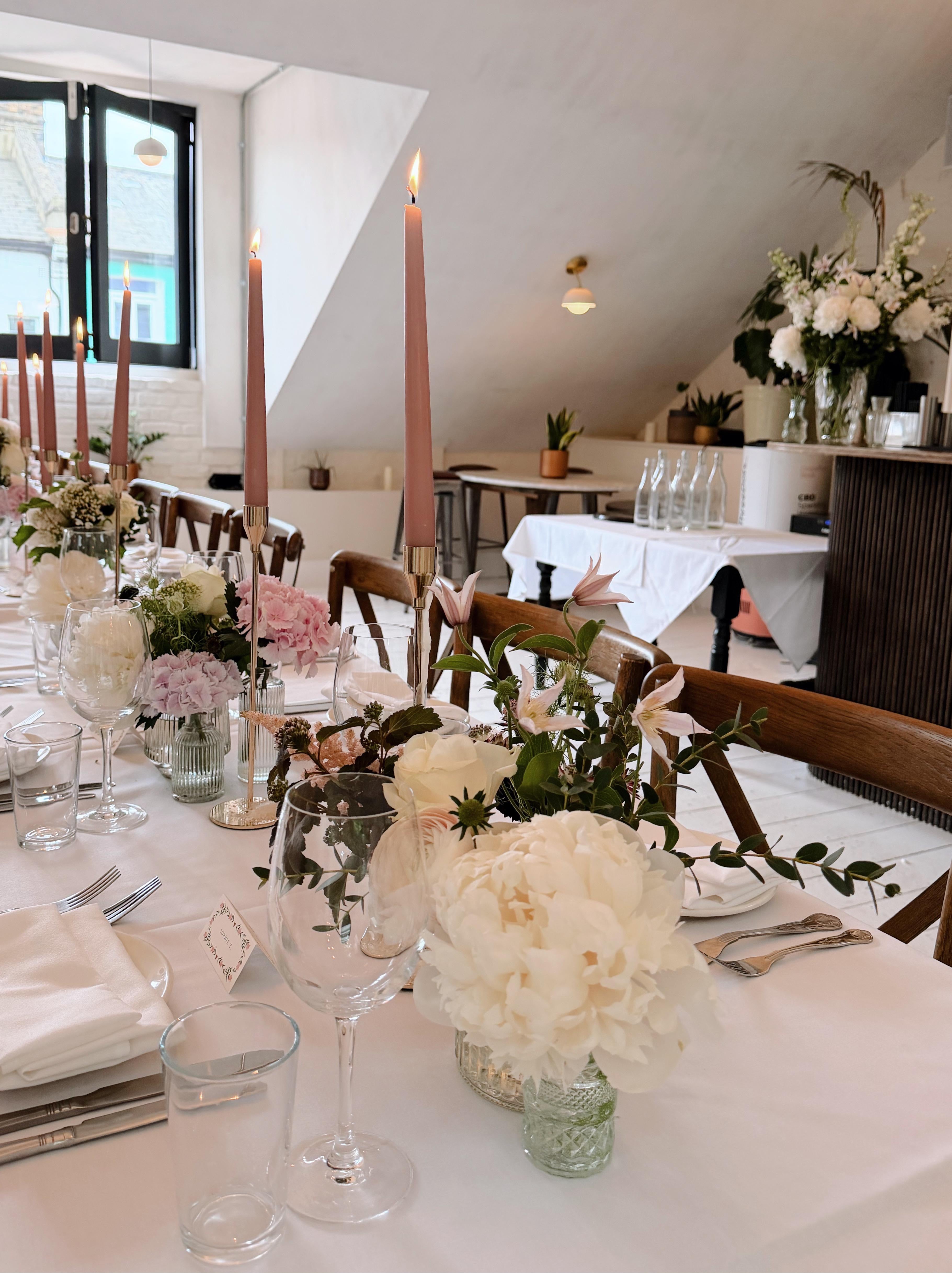 Elegant dining table setting with floral arrangements and candles in a well-lit room.